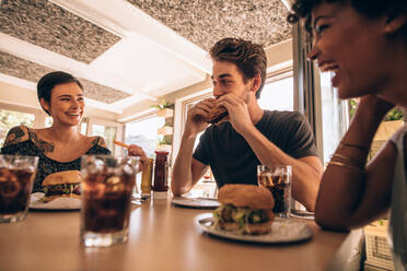 Eine Gruppe von Freunden trifft sich in einem Fast-Food-Restaurant. Ein Mann und eine Frau unterhalten sich und essen einen Burger in einem Restaurant. - JLPSF23131