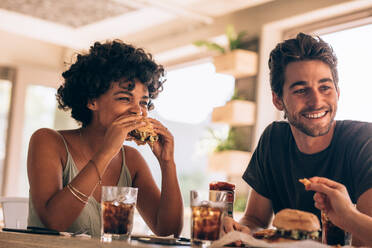 Junge Frau mit Freunden isst Burger in einem Restaurant. Junge Leute hängen in einem Café ab, unterhalten sich und essen Burger. - JLPSF23135