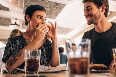 Frau hängt mit ihrem Freund ab und isst Burger. Paar sitzt im Restaurant am Tisch und isst Burger. - JLPSF23138