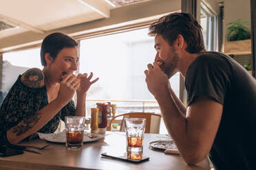 Junges Paar isst Burger zusammen. Lächelnde Frau isst Burger mit ihrem Freund in einem Restaurant. - JLPSF23142