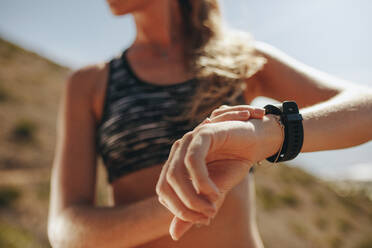 Läuferin, die ihren Fitnessfortschritt auf ihrer Smartwatch überprüft. Nahaufnahme einer Frau, die eine Fitness-App nutzt, um ihre Trainingsleistung zu überwachen, während sie auf einem Bergpfad trainiert. - JLPSF23161