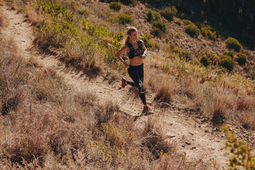 Draufsicht auf eine junge Frau, die auf einem Feldweg läuft. Fitness-Frau, die durch einen Bergpfad läuft. - JLPSF23170