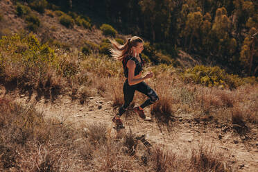 Fit young woman running on mountain trail. Woman trail runner training for cross country run. - JLPSF23171