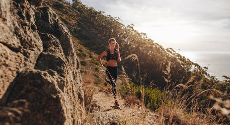 Woman running over extreme terrain on the hillside. Female runner training outdoors on rocky mountain trail. - JLPSF23172