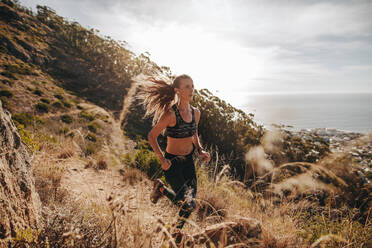Sportliche Frau, die für einen Langlauf über einen Bergpfad trainiert. Frau läuft über einen felsigen Pfad am Hang. - JLPSF23174
