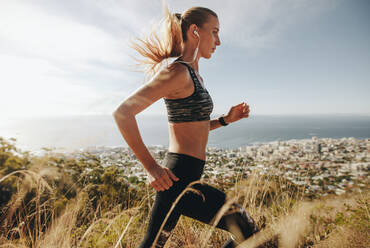 Seitenansicht einer jungen Frau in Sportkleidung, die durch extremes Gelände auf einem Berg läuft. Eine Läuferin trainiert für einen Langlauf. - JLPSF23175