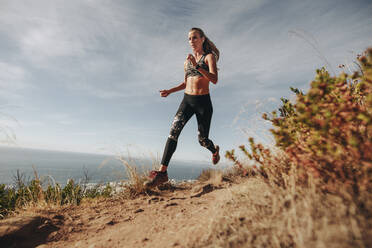 Fit sports woman sprinting over rocky trail on mountain. Woman running downhill on mountain path. - JLPSF23179