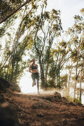 Sporty woman running on country trail. Female athlete running through mountain path with trees in background. - JLPSF23182