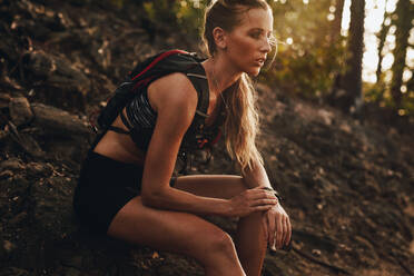 Female athlete relaxing after a run. Woman taking a break from exercise and relaxing on mountain trail. - JLPSF23192