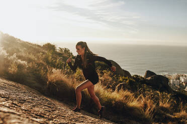 Fit young woman running up a rocky mountain trail. Woman trail runner training for uphill run. - JLPSF23199