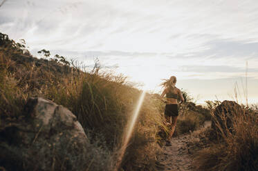 Rückansicht einer Sportlerin beim Trailrunning auf einem Bergpfad. Läuferin beim Training in der schönen Natur an einem sonnigen Tag. - JLPSF23202