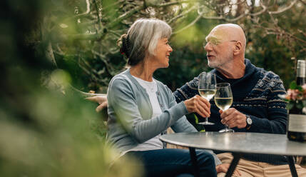 Alter Mann und Frau, die Zeit miteinander verbringen und Wein trinken. Altes Paar, das zusammen in einem Garten sitzt und Weingläser hält und sich gegenseitig ansieht. - JLPSF23203