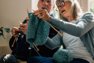 Ältere Frau, die ihrem Mann das Stricken von Wollkleidung beibringt. Älterer Mann, der von seiner Frau, die zu Hause sitzt, das Stricken von Wollkleidung lernt. - JLPSF23212