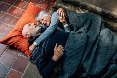 Älteres Paar, das auf dem Boden liegt, sich gegenseitig umarmt und spricht. Alter Mann und Frau, die zu Hause auf dem Boden schlafen, eine Decke abdecken und sich unterhalten. - JLPSF23215
