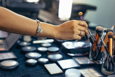 Make-up-Künstlerin nimmt einen Pinsel für Make-up. Make-up-Pinsel und Grundierung Schattierungen auf dem Tisch in einem Make-up-Raum angeordnet. - JLPSF23235