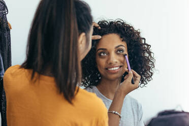 Makeup artist shading under the eyes to remove dark circles. Model undergoing makeup getting ready for photo shoot. - JLPSF23236