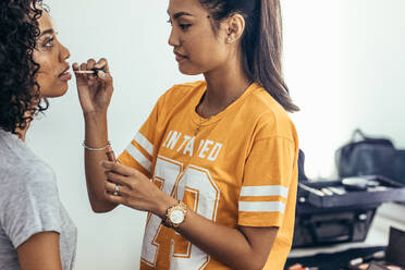 Seitenansicht einer Visagistin, die einem Modell Lippenfarbe aufträgt. Modell bereitet sich auf ein Fotoshooting vor. - JLPSF23237