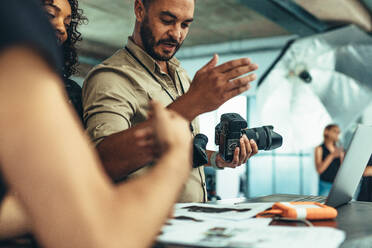 Fotograf mit Digitalkamera bei der Überprüfung des Fotoshootings. Fotograf bespricht Ideen mit seinem Team während des Fotoshootings. - JLPSF23242