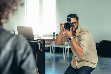 Fotograf bei einem Fotoshooting mit einer an einen Laptop angeschlossenen Digitalkamera. Fotograf in Aufnahmeposition. - JLPSF23254