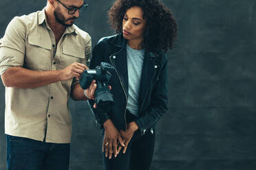 Photographer talking about the shoot with the model showing the image in camera. Studio shot of a photographer and a female model on a black background. - JLPSF23264