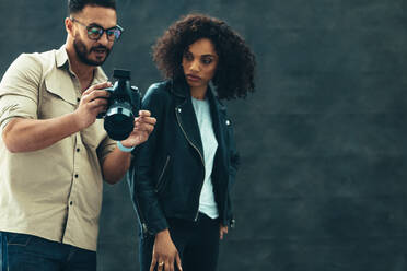 Ein Fotograf bespricht mit einem weiblichen Modell während eines Fotoshootings einen Punkt. Studioaufnahme eines Fotografen, der einem Modell seine Kamera zeigt. - JLPSF23265