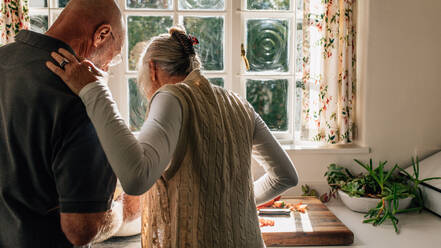 Rückansicht eines älteren Paares, das zusammen in der Küche steht und Essen kocht. Ältere Frau beobachtet ihren Mann beim Kochen in der Küche stehend. - JLPSF23278