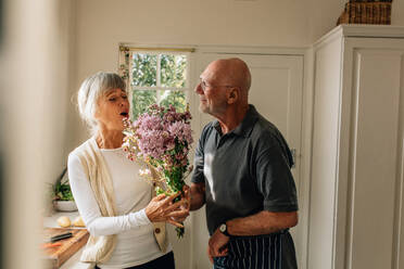 Ein Mann drückt seine Liebe zu seiner Frau aus, indem er ihr zu Hause einen Blumenstrauß schenkt. Eine ältere Frau freut sich, dass ihr Mann ihr einen Blumenstrauß schenkt. - JLPSF23283