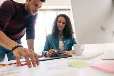 Businessman looking at business papers while the woman is writing on the digital writing pad. Business partners working together in office. - JLPSF23359