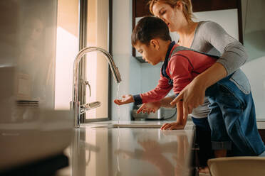 Kleiner Junge mit Mutter beim Händewaschen in der Spüle. Frau hilft ihrem Sohn beim Händewaschen in der Spüle nach dem Kochen. - JLPSF23377