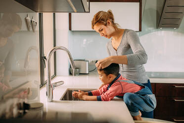 Fürsorgliche Mutter und Kind waschen sich die Hände in einem Waschbecken in der Küche. Kleiner Junge mit Mutter wäscht sich die Hände unter dem Wasserhahn der Spüle. - JLPSF23378