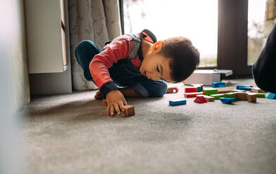 Kleiner Junge spielt mit bunten Holzklötzen auf einem Boden im Innenbereich. Kind spielt mit Spielzeug zu Hause. - JLPSF23381