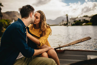 Young couple on a romantic date sitting in a boat and kissing. Couple in love sitting in a boat kissing with eyes closed holding each other. - JLPSF23402