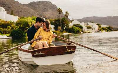 Romantisches Paar sitzt in einem Boot und berührt sich. Paar auf einem Boot Datum in einem See mit Hügeln und Häusern im Hintergrund. - JLPSF23404