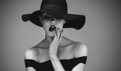 Modeporträt einer sinnlichen Frau mit Hut, die ihre Lippen berührt. Flirty elegante Frau in schwarz und weiß. - JLPSF23419