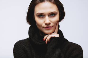 Close up Porträt der schönen Frau trägt schwarzen Pullover mit ihrer Hand auf dem Kinn. kaukasischen weiblichen Modell starrt in die Kamera. - JLPSF23421