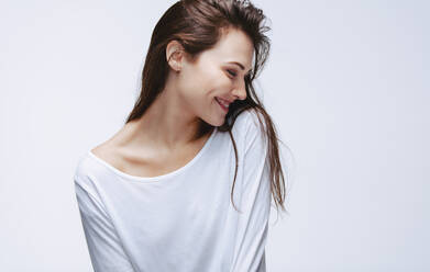 Schöne Frau in weißem Top lächelnd mit geschlossenen Augen. Glückliches weibliches Model in Freizeitkleidung auf weißem Hintergrund. - JLPSF23437