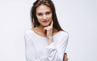 Portrait of attractive woman with finger on cheek staring at camera. Beautiful caucasian female model against white background. - JLPSF23438