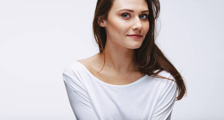 Porträt eines schönen weiblichen Modells vor weißem Hintergrund. Attraktive Frau in weißem Oberteil schaut in die Kamera. - JLPSF23439