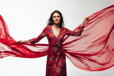 Kaukasisches weibliches Modell in rotem fliegenden Kleid im Studio. Junge Frau posiert in schönem Kleid auf weißem Hintergrund. - JLPSF23441