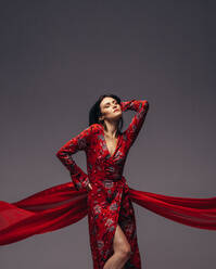 Sinnliche Frau posiert in rotem Kleid vor grauem Hintergrund. Weibliches Modell trägt schönes Kleid. - JLPSF23443