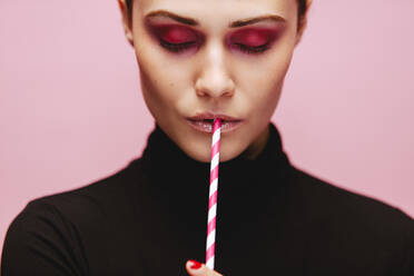 Close up von schönen jungen weiblichen Modell mit ihren Augen geschlossen hält einen Strohhalm trinken. Kaukasische Frau mit professionellen Make-up auf rosa Hintergrund mit Stroh zu trinken. - JLPSF23448