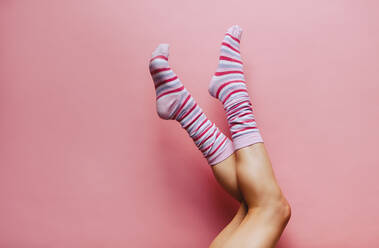 Frauenbeine in bunten gestreiften Socken auf rosa Hintergrund. Füße der Frau in Socken hochgehoben. - JLPSF23462