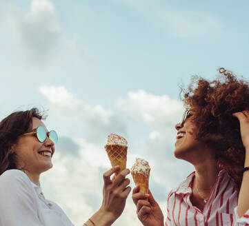 Zwei junge Frauen stehen mit Eiswaffeln zusammen. Glückliche junge Freundinnen essen Eis im Freien. - JLPSF23492