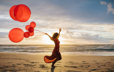 Young beautiful woman running on the beach holding balloons. Woman with balloons on the beach enjoying a summer day. - JLPSF23494