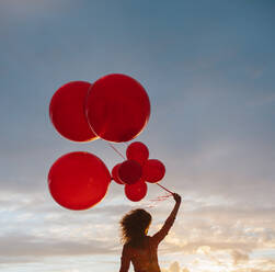 Rückansicht einer Frau gegen den Himmel mit einem Bündel Luftballons. Frau mit Luftballons bei Sonnenuntergang. - JLPSF23497