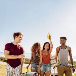 Eine Gruppe von Männern und Frauen, die mit einem Bier im Freien spazieren gehen. Freunde, die eine schöne Zeit miteinander verbringen. Junge Leute, die an einem Sommertag ein Picknick machen. - JLPSF23502