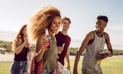 Attractive woman having beer while walking with friends outdoors. Female hanging out with group of friends on a summer day. - JLPSF23513