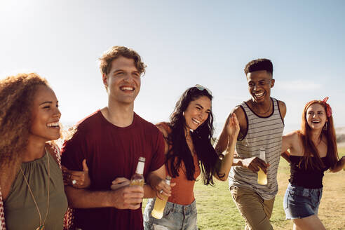 Eine gemischtrassige Gruppe junger Leute, die sich an einem Sommertag im Freien vergnügt. Junge Männer und Frauen mit Bieren gehen zusammen. - JLPSF23517