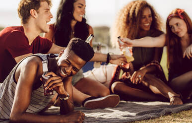 Fröhlicher junger Afrikaner, der mit Freunden im Freien sitzt und lacht. Ein Mann genießt ein Sommerwochenende mit Freunden. - JLPSF23527