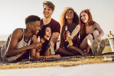 Eine Gruppe verschiedener junger Leute, die sich im Freien bei einem Getränk entspannen. Junge Männer und Frauen hängen ab, unterhalten sich, trinken Bier und lachen. - JLPSF23529